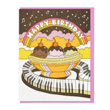 The "Happy Birthday Musical Banana Split" card by Lucky Horse Press features a banana split, keyboard path, rainbow, and "Happy Birthday" text on a colorful background. Made in the USA with a recycled cover.