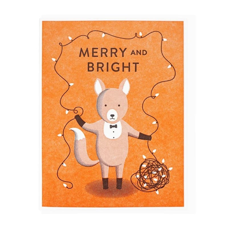 The Cards | Merry & Bright Fox by Lucky Horse Press features a fox in a tuxedo holding festive lights with "Merry and Bright" on an orange background. This letterpress card brings charm to any holiday occasion.