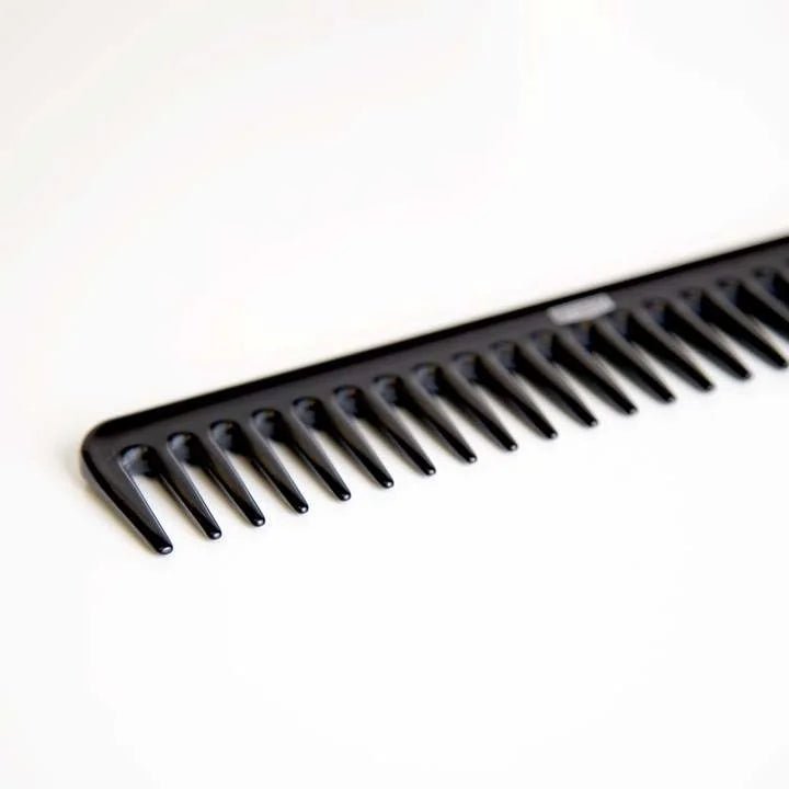 The Uppercut Deluxe CB11 Rake Comb by Uppercut Deluxe, featuring wide teeth and a black finish, is displayed at an angle on a white surface.