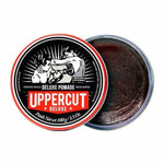 A round tin of Uppercut Deluxe Deluxe Pomade displays a vintage boxing illustration on the lid; inside, the open container reveals dark, high-shine pomade.