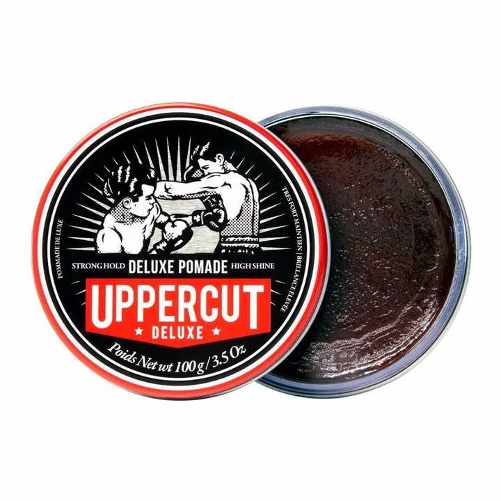 An open tin of Uppercut Deluxe’s Deluxe Pomade displays the product, with its lid featuring two boxers and product details.
