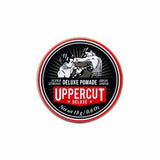An 18g (0.6 oz) round tin of Uppercut Deluxe's Deluxe Pomade, a strong hold, high shine pomade featuring two boxer illustrations and branding by Uppercut Deluxe.