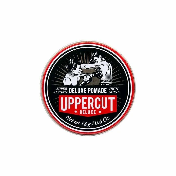 An 18g (0.6 oz) round tin of Uppercut Deluxe's Deluxe Pomade, a strong hold, high shine pomade featuring two boxer illustrations and branding by Uppercut Deluxe.