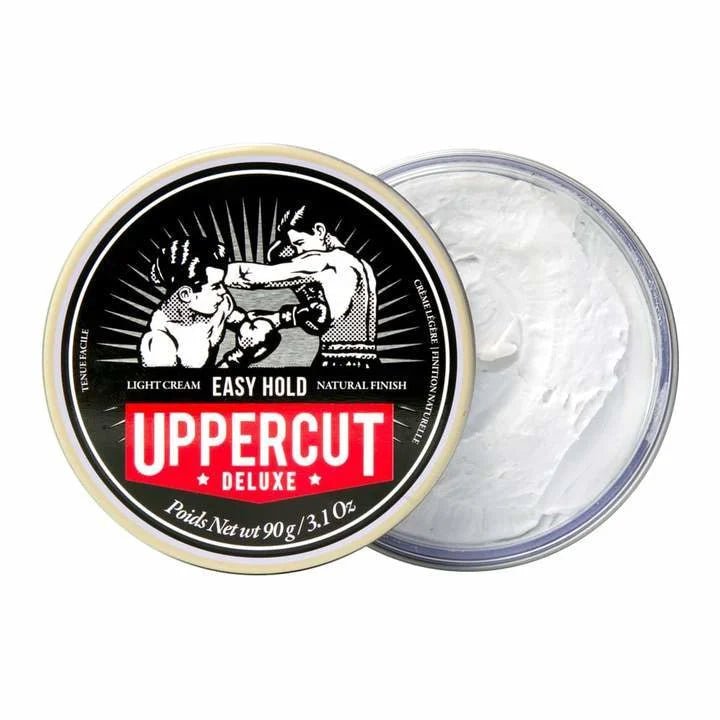 A round Uppercut Deluxe Easy Hold container with the lid off reveals light cream inside; the lid shows two boxers and product details. This styling product delivers a natural, matte finish for effortless hair styling.