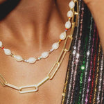 A close-up of a person wearing the Edith Necklace by Larissa Loden, a freshwater pearl piece layered with a chunky gold chain and gold fill beads, paired with a multicolored sequined garment.