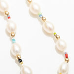 A close-up of the Edith Necklace by Larissa Loden, showcasing oval freshwater pearls, gold fill beads, and colorful African Christmas beads on a white background.