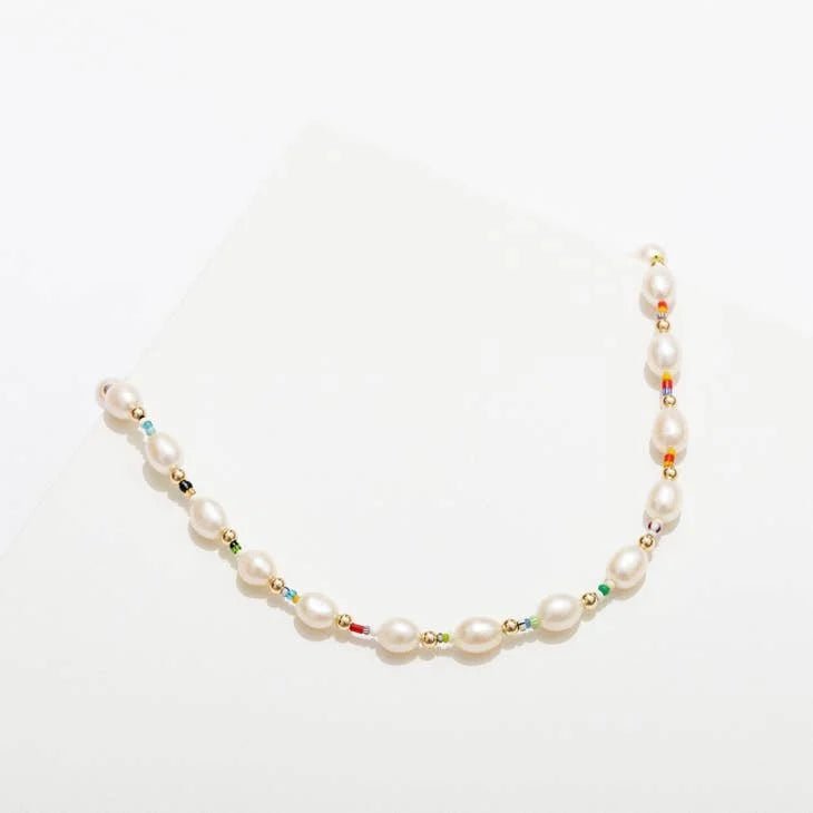The Edith Necklace by Larissa Loden features white oval freshwater pearls, multicolored African Christmas beads, and gold fill beads arranged delicately on a white background.