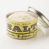 An open tin of "Friends Forever Sea Salt" by Beautiful Briny Sea, filled with coarse salt. The label suggests a salty-sweet blend, combining sea salt with honey and the phrase "friends forever.