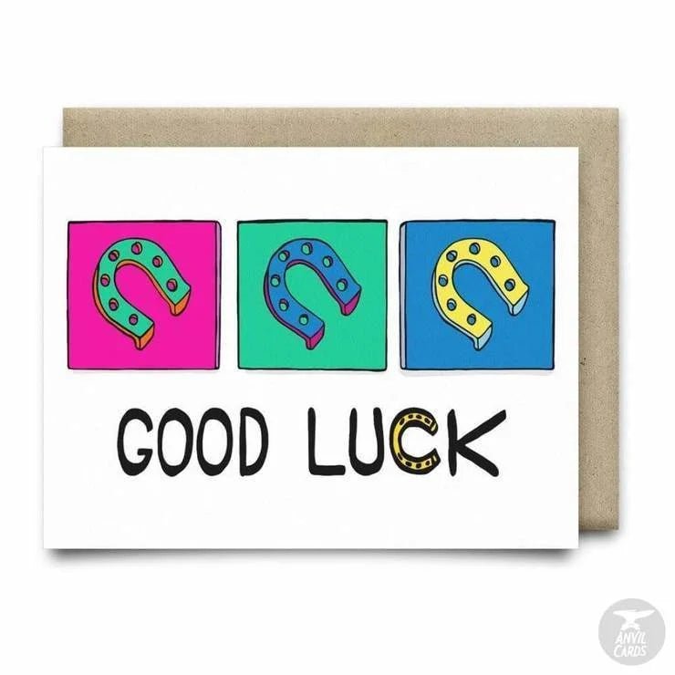 The Anvil Cards Good Luck Greeting Card by Anvil Cards features three vibrant horseshoes above the words “GOOD LUCK,” with the letter “U” creatively replaced by a yellow horseshoe. Printed on premium linen paper, this A2 card is blank inside for your personal message.