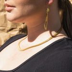 Close-up of a woman wearing the Grace Necklace by Larissa Loden and a gold drop earring, shown from chin to shoulder, dressed in a black top.