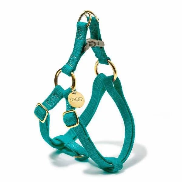 The Found My Animal Harness is a teal handmade pet harness with gold metal rings, a buckle, and a round ID tag engraved "FOUND," shown on a white background.