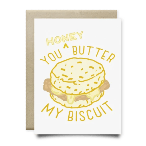 The Honey You Butter My Biscuit Card by Anvil Cards features a biscuit sandwich illustration and yellow text. This A2 card is blank inside and comes with an envelope placed behind it.