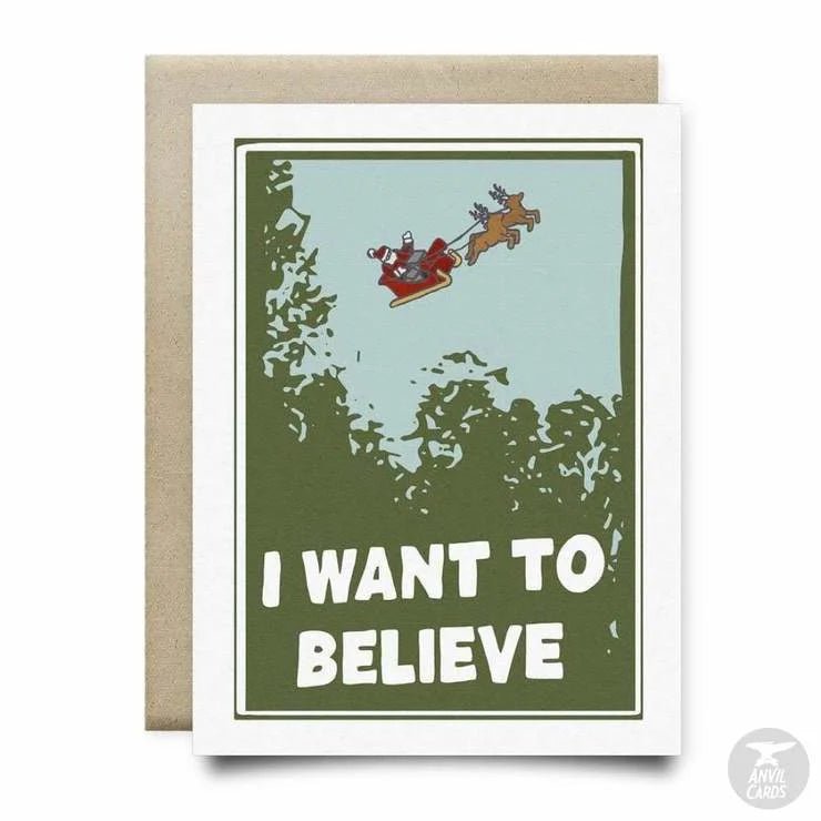 The "I Want To Believe (in Santa) Card" by Anvil Cards is an A2 greeting card featuring Santa in his sleigh with reindeer above trees and "I WANT TO BELIEVE" printed on textured linen paper. The inside is blank.