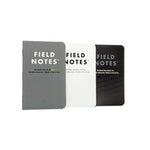 Three Field Notes "Ignition" notebooks by Field Notes, in gray, white, and black covers, are side by side on a white background. Each shows its type and page details—ideal for bullet journaling or checklist use.