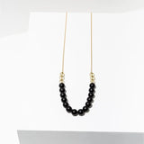 The Isles Necklace by Larissa Loden features a handmade matte gold chain with eight black matte gemstone beads and three gold beads on each side, shown on a white background.