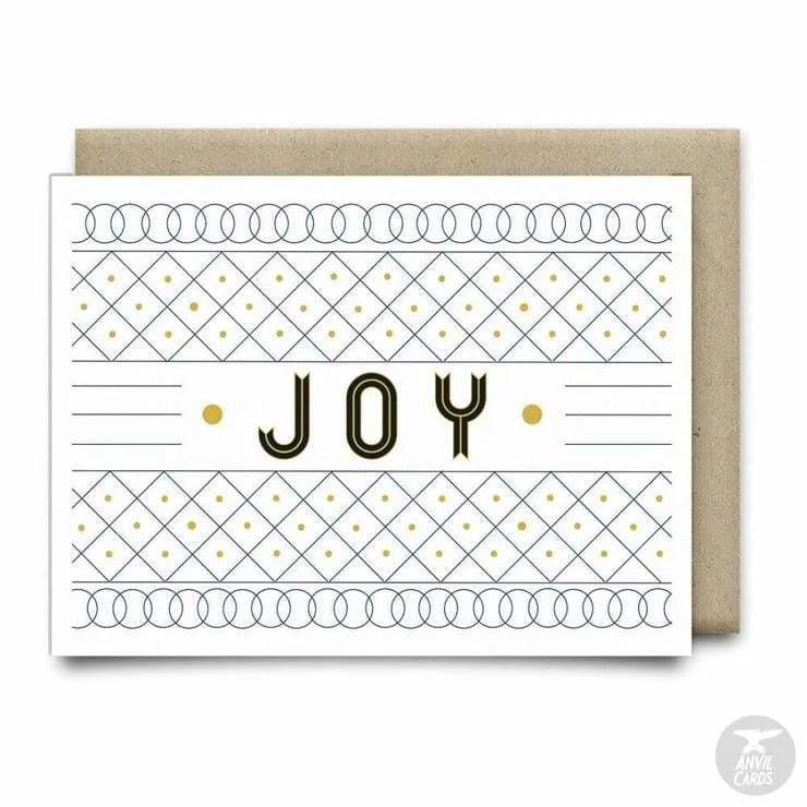 The Joy Christmas Card by Anvil Cards is a blank A2 greeting card featuring "JOY" in bold with geometric patterns and gold dots on luxe linen paper, paired with a brown envelope.