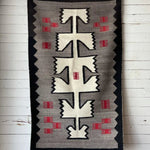 The Vintage Klagetoh Rug Circa 1950 features classic black, white, gray, and red geometric patterns, hanging on a white wooden wall to display the enduring beauty of traditional Navajo weaving.