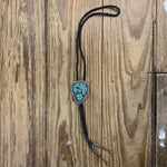 The Vintage Large Turquoise Bolo features a braided black leather tie with a triangular turquoise and silver slide, displayed on a weathered wooden surface.