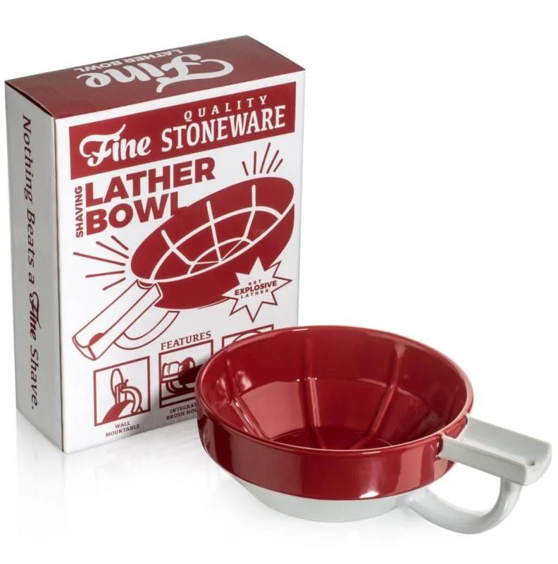 The red and white Fine Accoutrements Lather Bowl sits next to its packaging, which features the product name, highlights its use with a shaving brush and traditional shaving soap, and displays an illustration of the bowl.