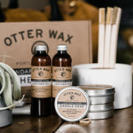 Otter Wax Leather Polishing Oil and other Otter Wax products, such as saddle soap and leather conditioner, are displayed on a table with branded packaging in the background.