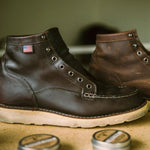 A pair of brown leather boots without laces sits on a surface, with tins of Otter Wax Leather Salve and shoe polish in the foreground.