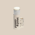 A tube of Poppy & Pout Lip Balm stands upright with the cap removed, showing the balm and a floral design on the cap against a beige background.