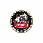 A round tin of Uppercut Deluxe Matte Pomade displays a black-and-white boxer illustration, with details highlighting its water-soluble formula, matte finish, medium hold, and net weight.