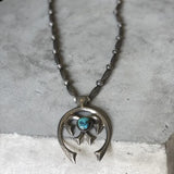 The Vintage Navajo Pearls with Turquoise Pendant necklace features a sterling silver chain and crescent-shaped turquoise pendant, elegantly displayed on a gray surface.