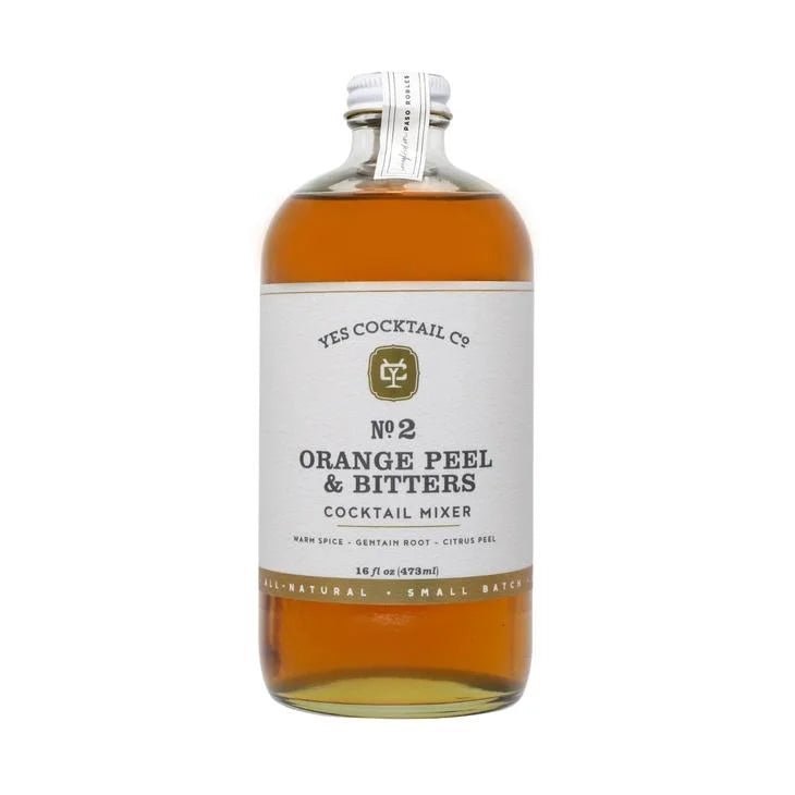 A clear glass bottle of Yes Cocktail Co.’s Orange Peel & Bitters Cocktail Mixer features a crisp white label and metal cap, containing amber liquid that recalls classic old fashioned flavors.