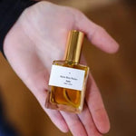 A person holds a small glass bottle of Saint Rita Parlor's Parfum | Signature, a unisex fragrance with a gold cap.