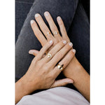 Two hands rest on crossed legs, each wearing several gold rings—including the JaxKelly Ring | Smokey Quartz Point; nails are natural and manicured.