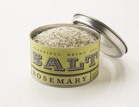 A partially open tin labeled "Rosemary Sea Salt | Beautiful Briny Sea" by Beautiful Briny Sea reveals coarse rosemary sea salt, an herbal seasoning.