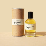 A clear glass bottle labeled "Sagebrush | Saguara Perfumes" (50 mL Eau de Parfum, vegan, with California sage notes) and its cylindrical cardboard container from Saguara Perfumes are displayed on a beige surface and background.
