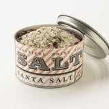 A tin of Santa Sea Salt by Beautiful Briny Sea sits open on a white surface, showing its coarse seasoning blend with organic rosemary and pink peppercorn.