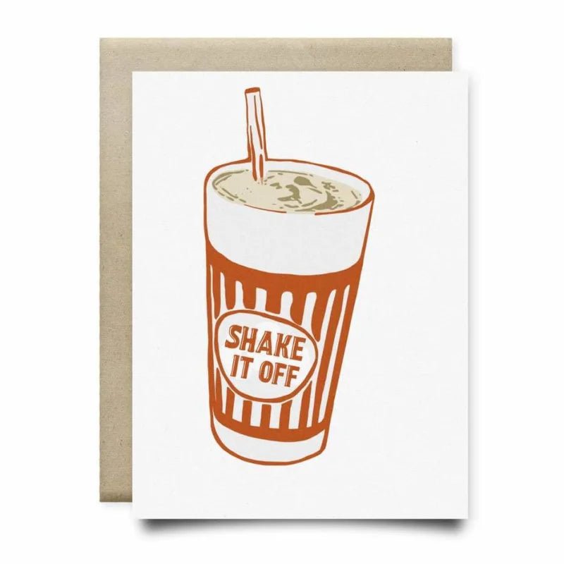 The Shake It Off Card by Anvil Cards features a milkshake cup with a straw and “SHAKE IT OFF” on the front, set on a brown envelope. This A2 greeting card is blank inside and printed on textured linen paper for an elegant touch.