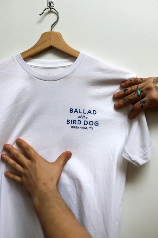 Person Holding White Shirt With Bald Dog Logo From Bird Dog Classic Shop.