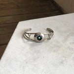 The Vintage Small Shadow Box Squash Blossom & Cuff, a sterling silver bracelet with a central round shadow box and dark star-shaped inlay, is displayed on a light surface.