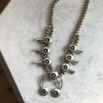 The Vintage Small Shadow Box Squash Blossom & Cuff, a sterling silver necklace with turquoise stones and subtle shadow box design, is displayed on a light-colored surface.