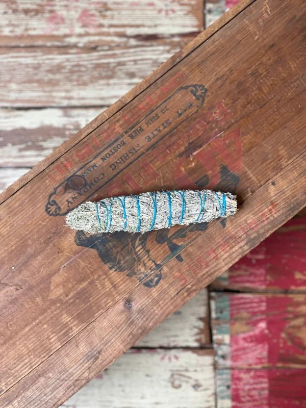 The Smudge Stick | Grandfather by Taos Herb Co. is wrapped with blue string and displayed on a vintage wooden box with faded labels and visible wood grain.