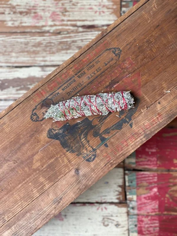 The Smudge Stick | Sage and Cedar from Taos Herb Co rests on a weathered wooden surface with faded paint, evoking the timeless traditions of Taos Pueblo.