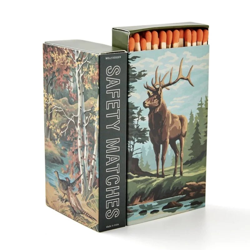 The Mollyjogger Stag 4" Safety Matches box displays wildlife art—a stag by a stream on the front and a forest bird on the side—while the partially opened box reveals 4-inch matches with match tips inside.