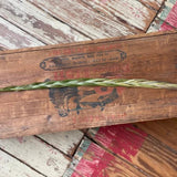 A single stalk of Sweetgrass from Taos Herb Co. is braided and set on a weathered wooden surface with faded paint and visible grain patterns.