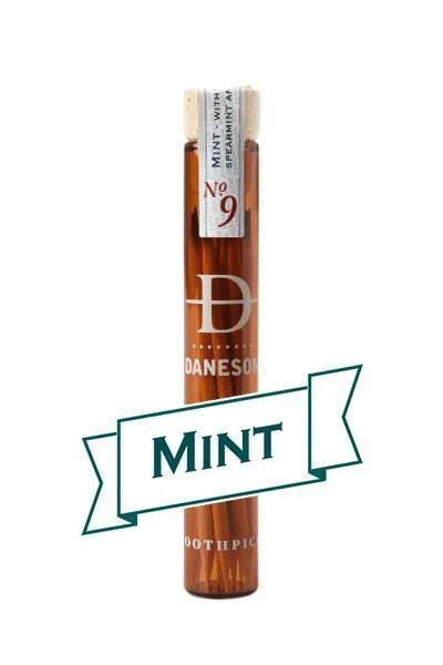 A glass vial labeled “Daneson Toothpick | Mint No. 09” holds essential oil-infused toothpicks with a cool mint flavor, featuring a "MINT" banner on the front.