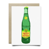 The Topo Happy Birthday Card by Anvil Cards is a blank A2 greeting card featuring a green glass bottle with a yellow "Happy Birthday" label, printed on linen paper, and includes an envelope placed behind the card.