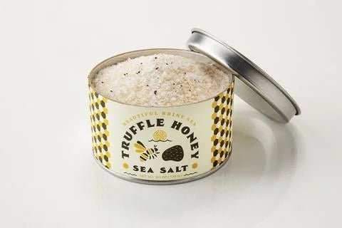 An open tin of Beautiful Briny Sea's Truffle Honey Sea Salt is filled with coarse, speckled salt infused with Italian black truffles, and its lid sits beside the container.