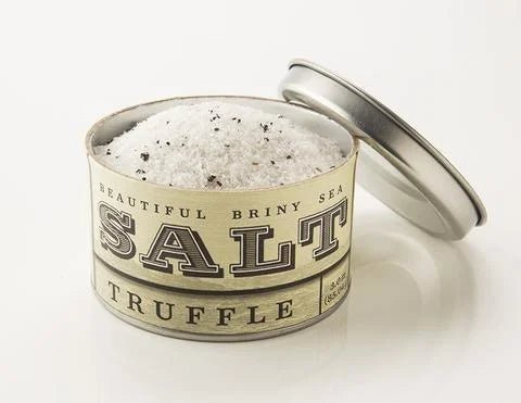 An open metal tin of Beautiful Briny Sea Truffle Sea Salt reveals coarse sea salt flecked with Italian black truffle pieces.