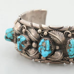 The Turquoise Watch Cuff by Vintage is a sterling silver bracelet with ornate leaf details and four large turquoise stones in bezel settings.