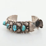 The Vintage Turquoise Watch Cuff is a sterling silver bracelet with intricate leaf details and four turquoise stones set along the front.