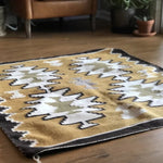 The Vintage Two Grey Hills Rug features a geometric Southwestern pattern in mustard yellow, white, olive green, and black, adding vintage style to your living room when placed on a wooden floor.