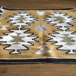 The Vintage Two Grey Hills Rug features a geometric, Navajo-inspired pattern in white, olive green, and gray on a mustard yellow background, shown here flat woven and displayed on a wooden floor.